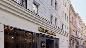 Un hotel llamado "HOTEL MEMORIES" con una fachada moderna, grandes ventanales y una entrada visible con asientos al aire libre.