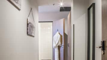 Un pasillo con suelo de madera, una bata colgada en una puerta y un cuadro enmarcado en la pared.