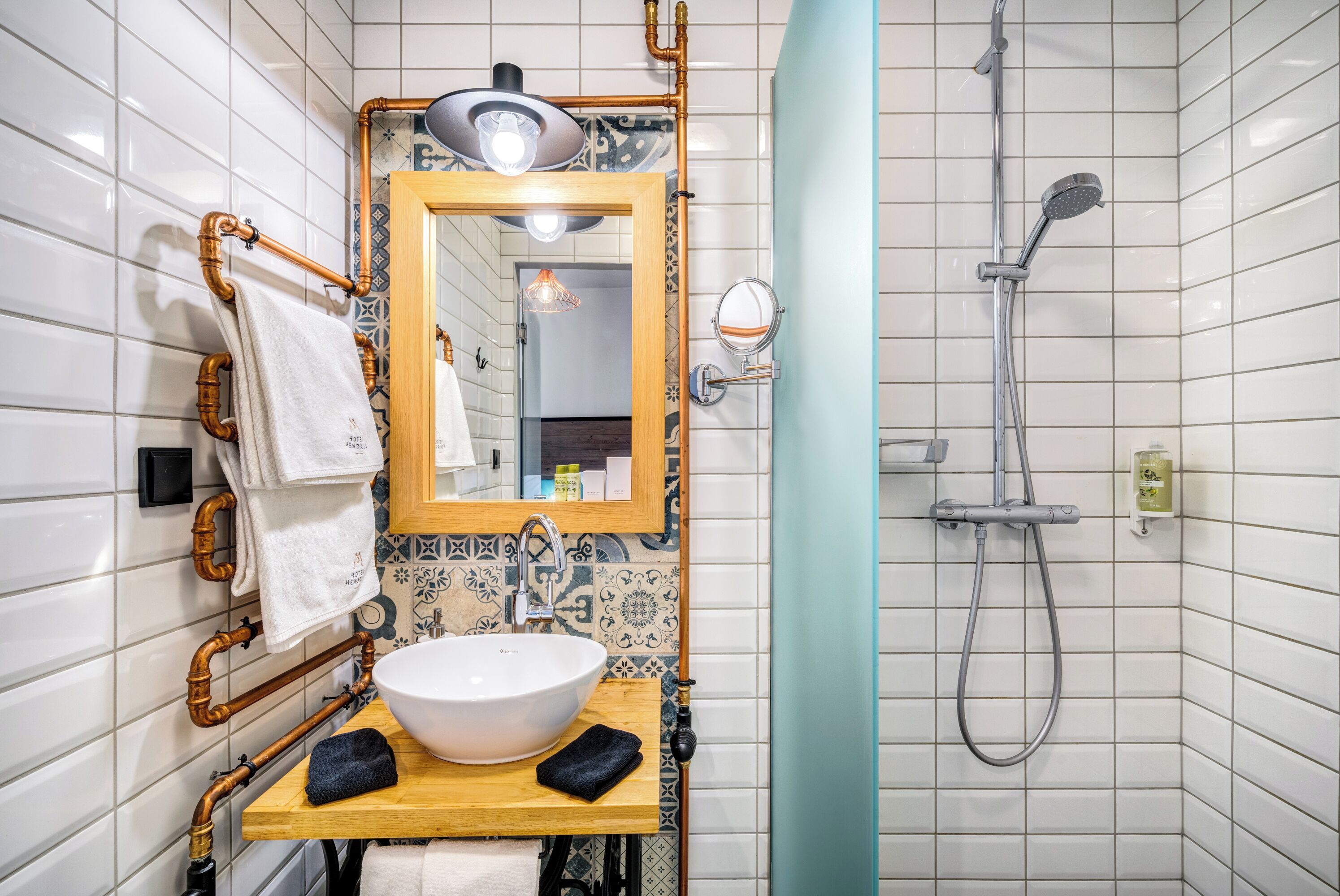 Un bagno con parete rivestita in piastrelle bianche, mobile lavabo in legno con lavandino bianco, uno specchio e una doccia.