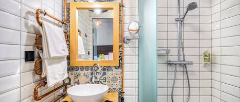 Un bagno con parete rivestita in piastrelle bianche, mobile lavabo in legno con lavandino bianco, uno specchio e una doccia.