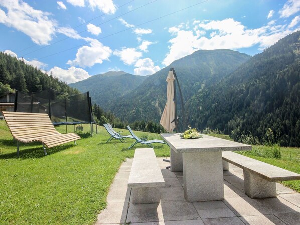 Relax in a serene outdoor seating area surrounded by lush green hills and a mountain range.