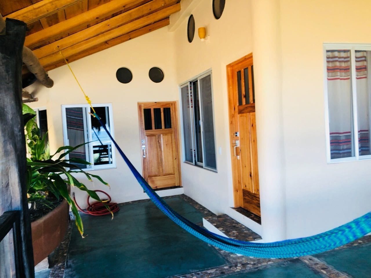 A covered outdoor area with a hammock, wooden doors, and a potted plant.