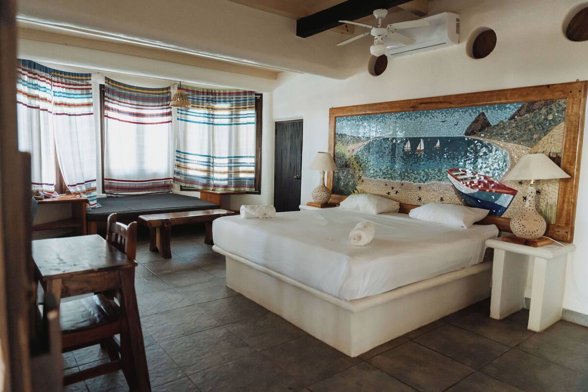 Um quarto espaçoso com uma cama grande, uma escrivaninha e um banco.