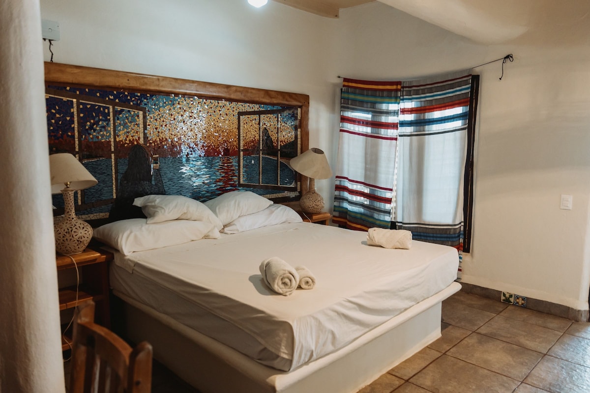 Cama com colchão branco, duas almofadas e uma toalha enrolada. Tem cabeceira de madeira com design em mosaico.