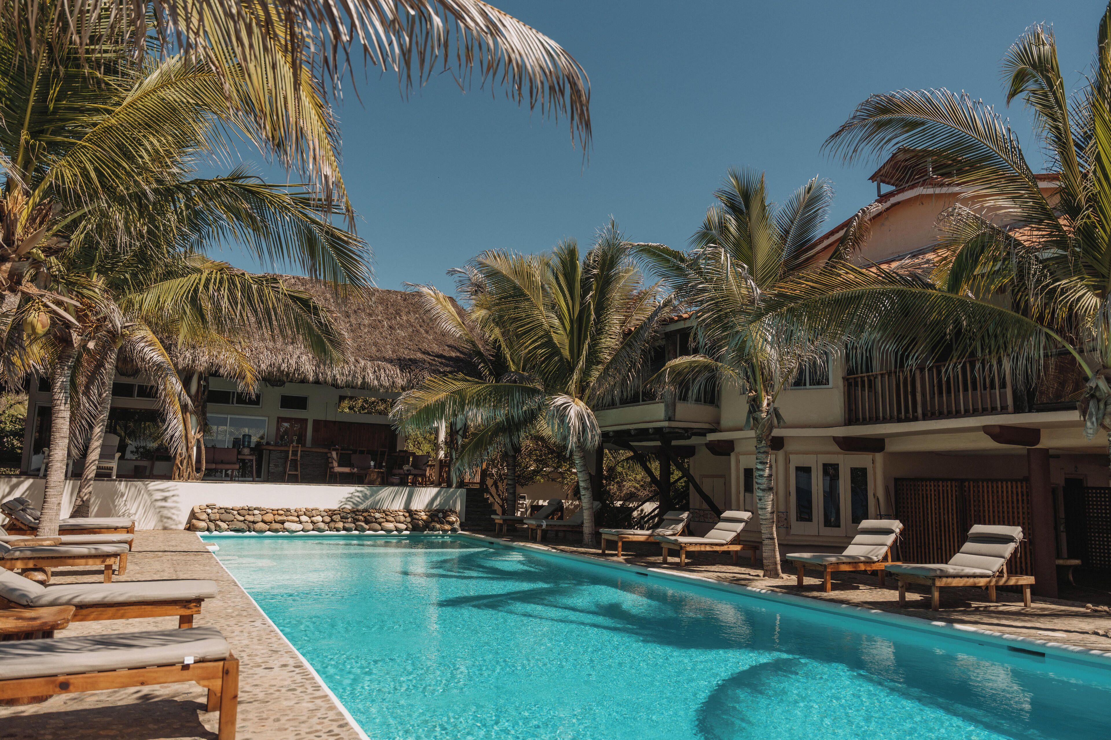 A pool area with lounge chairs, palm trees, and a building with a balcony.