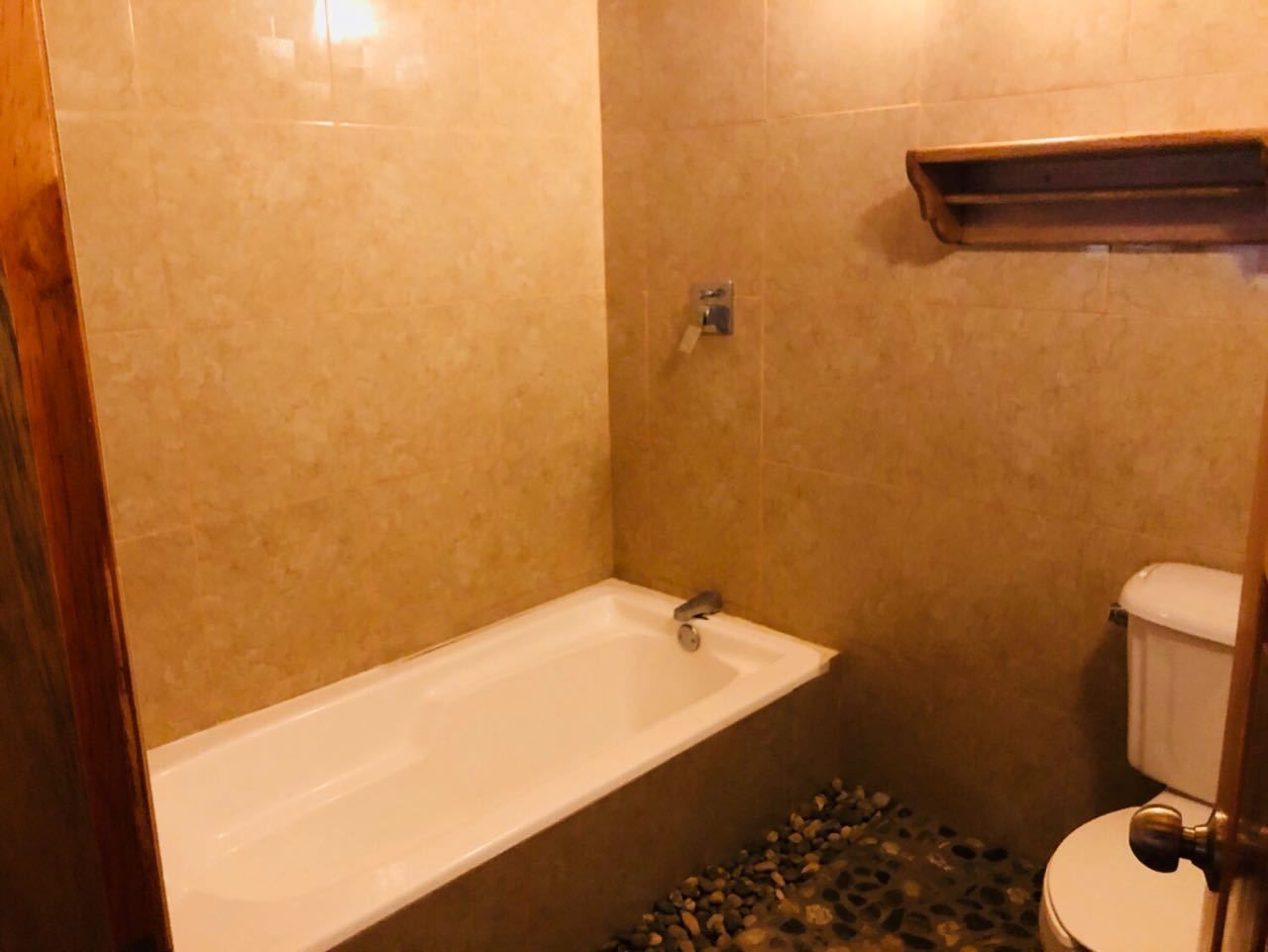 A bathroom with a bathtub, toilet, and a shelf above the toilet.