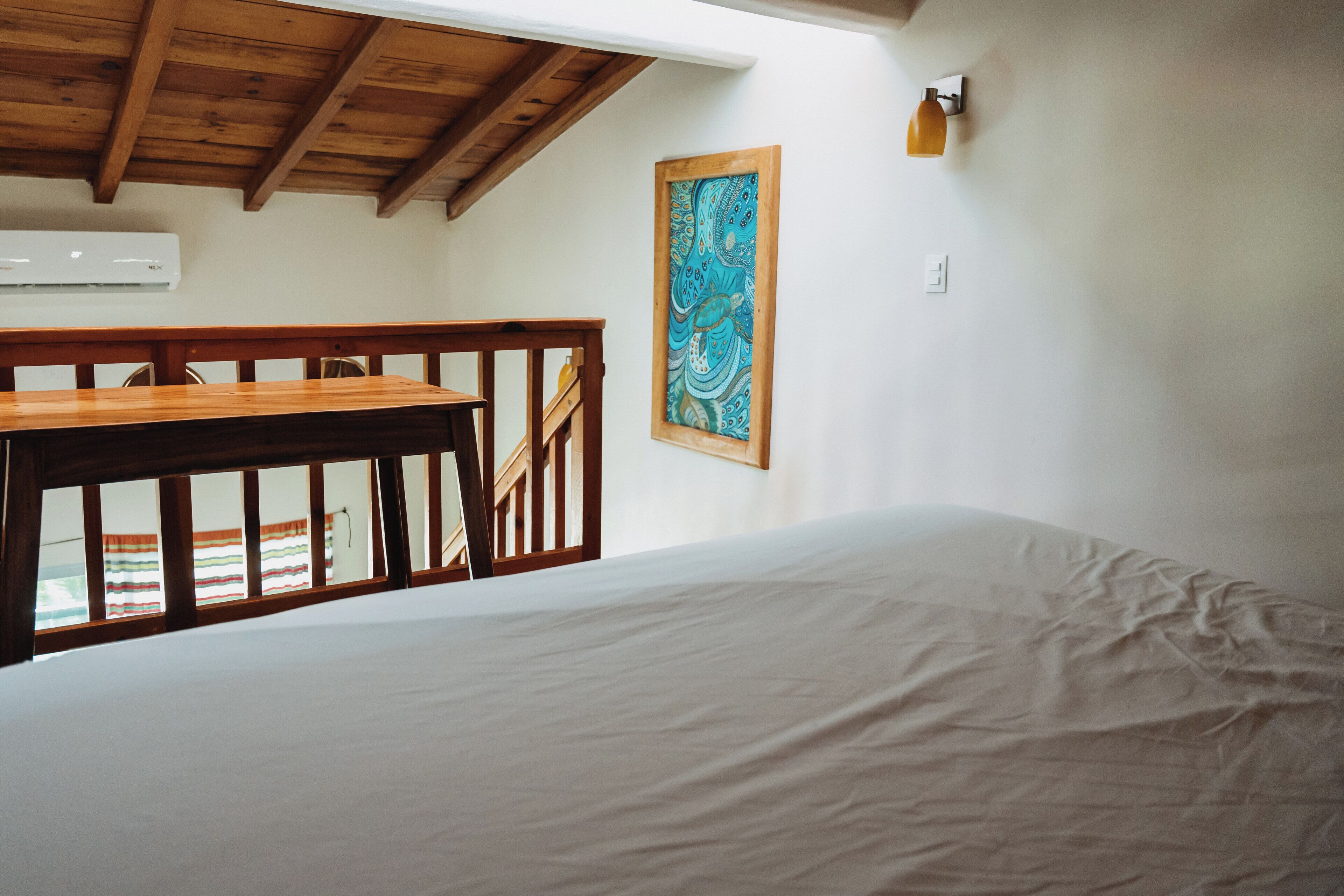 A bedroom with a wooden bed, a white mattress, a wooden table, and a colorful artwork on the wall.