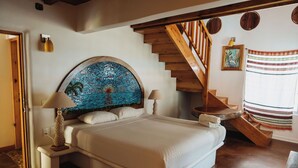 Ett sovrum med en stor säng, en trätrappa och en sänggavel i mosaik.