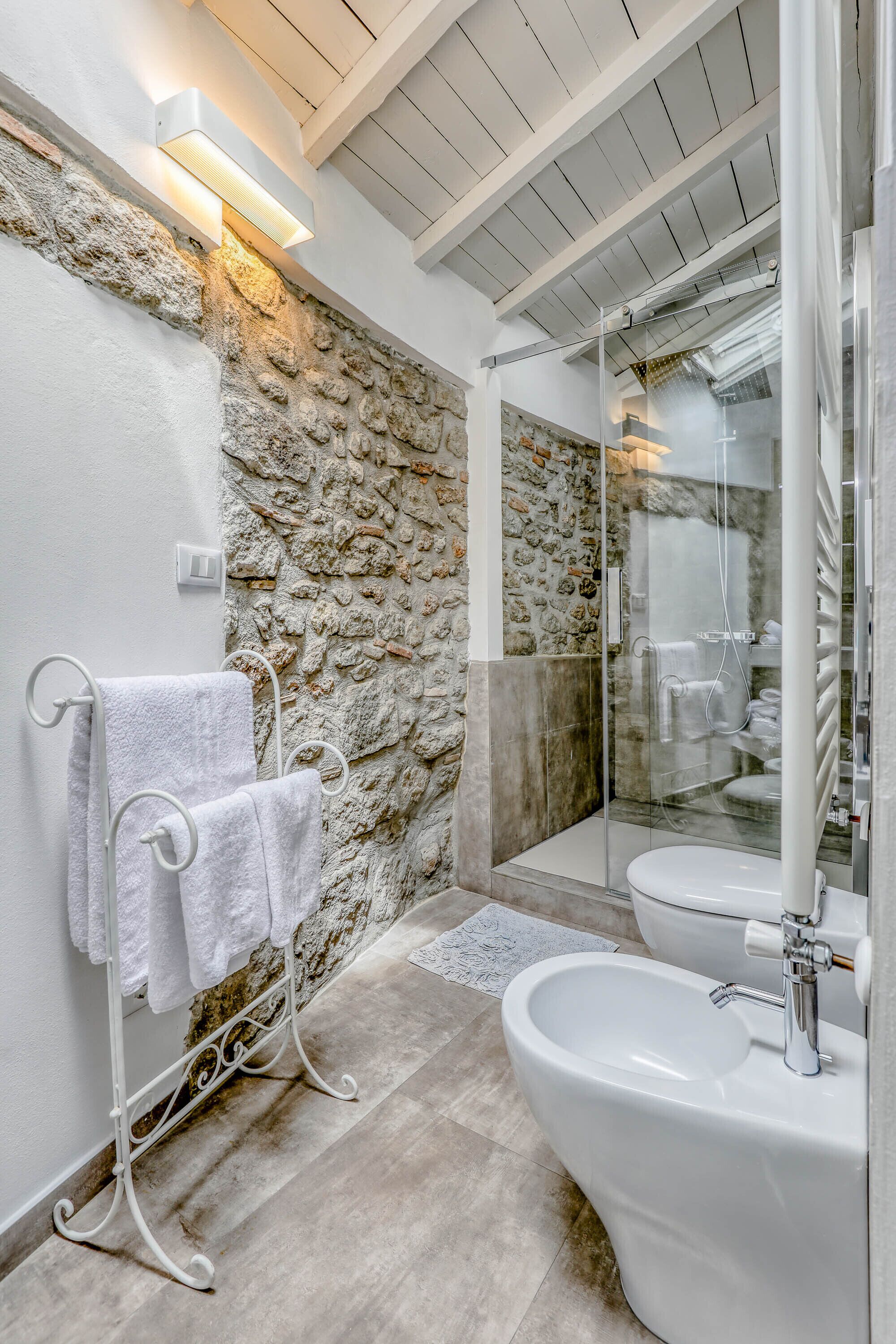 A bathroom with a stone wall, a glass shower enclosure, a white sink, and a towel rack.