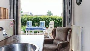 Una habitación con lavamanos, una silla, una mesa y vistas a un jardín con seto y sillas.
