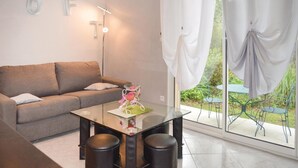 A modern living room with a glass-top table, two black stools, a sofa, and a view of a garden through large windows with curtains. - Awesome home in Ville di Paraso with WiFi (Ville di Paraso)