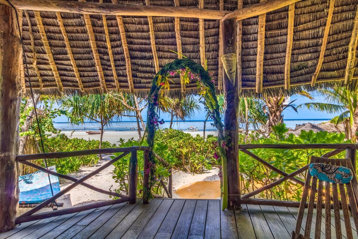 A wooden deck with a thatched roof overlooking a beach.
