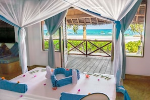 A room with a bed, a view of the beach, and a thatched roof structure.