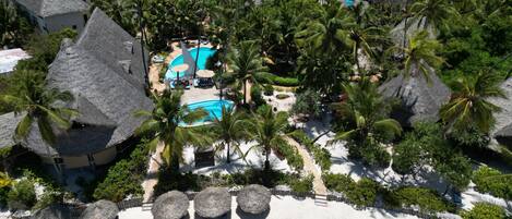 Ein Resort mit Pool, umgeben von Palmen und Gebäuden mit Strohdächern.