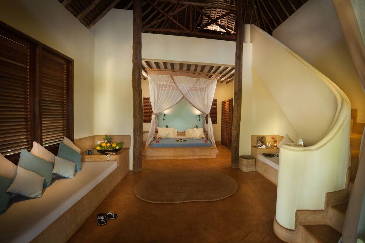 A bedroom with a bed, a sofa, a staircase, and a large window.