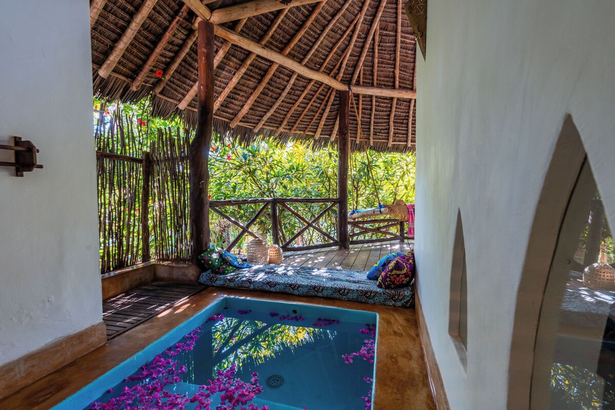 A pool with water lilies, a wooden deck, and a thatched roof structure.