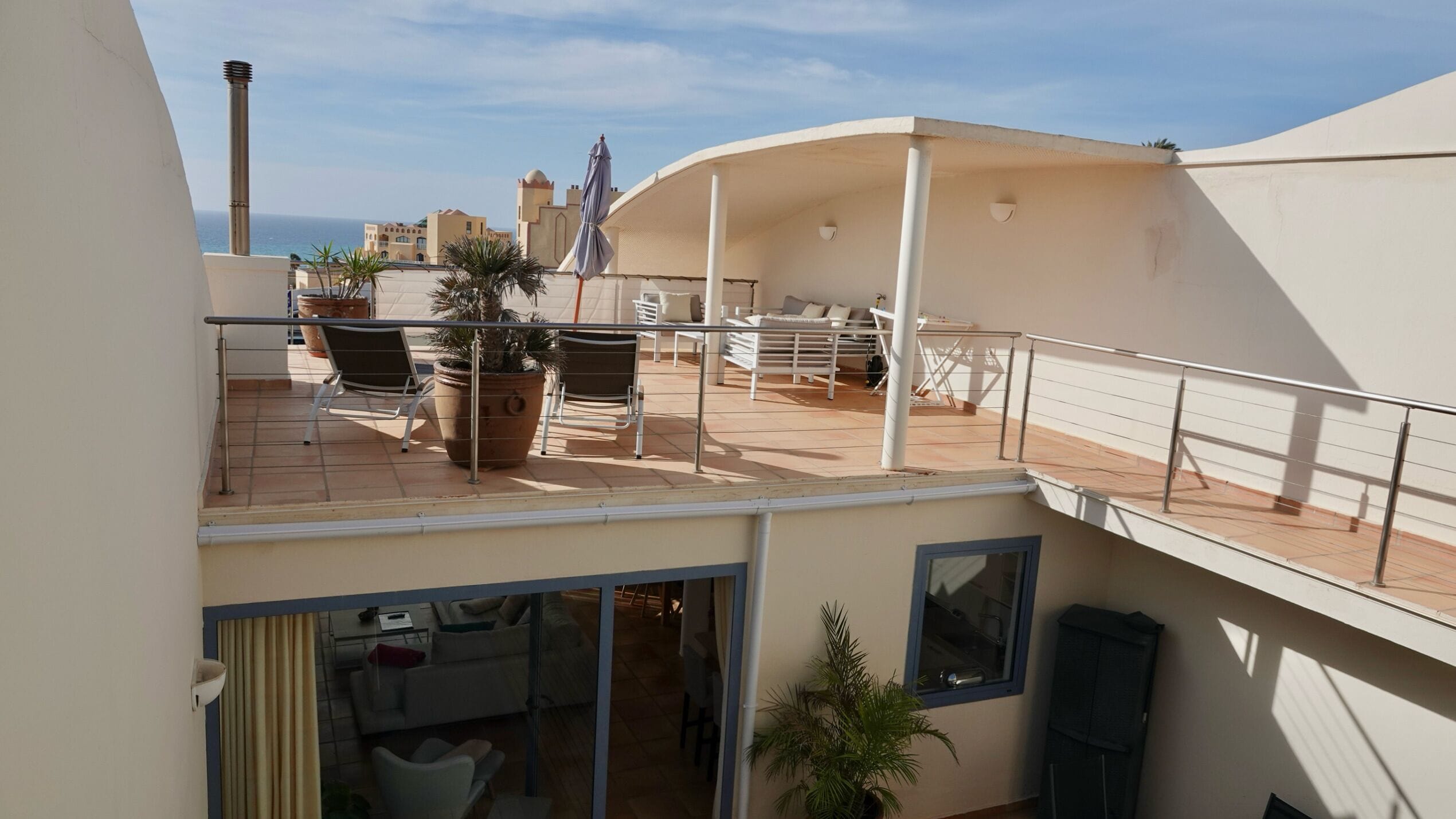 Une terrasse sur le toit avec des sièges en plein air, une vue sur la mer et, en arrière-plan, un bâtiment doté d’une structure en forme de dôme.