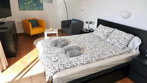 Ein modernes Schlafzimmer mit einem großen Bett, einer Sitzecke, einem Schreibtisch und einem Fernseher.