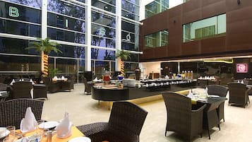 A spacious indoor area with wicker furniture, a buffet setup, and large windows offering views of the outside.