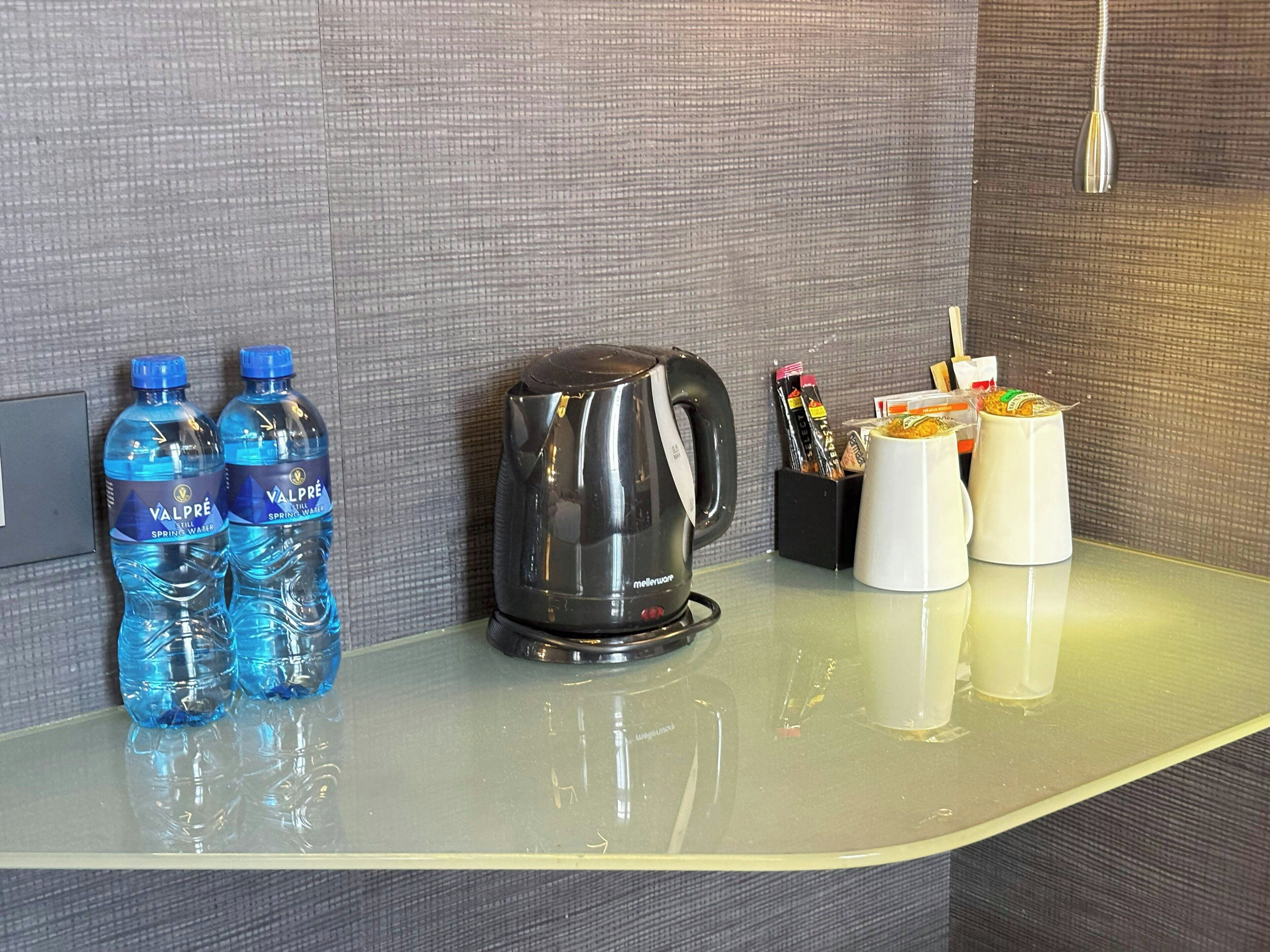 A hotel room counter with two bottles of water, a coffee maker, and a mug.