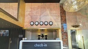 Ein Hotel-Empfangsbereich mit einer Rezeption, Uhren, die verschiedene Zeitzonen anzeigen, und einer großen Chandelier.