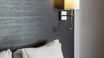 A hotel room with a bed, white pillows, a headboard with a textured pattern, and a wall-mounted light fixture.