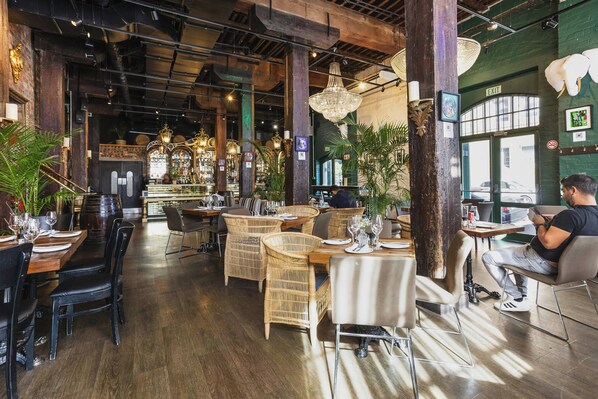 Un interior de restaurante con mesas de madera, sillas de mimbre y candelabros colgantes.