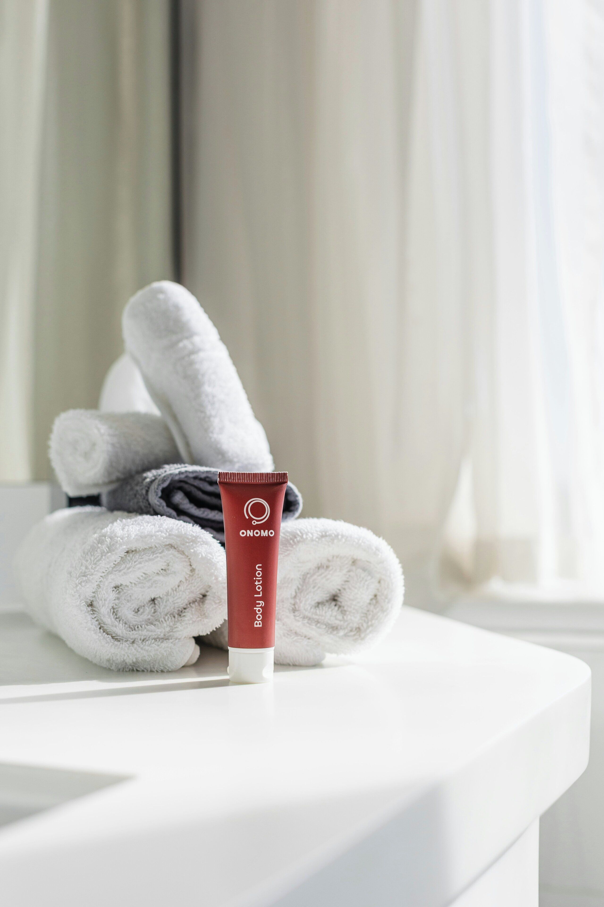A bathroom with a white sink, a rolled white towel, and a red tube of body lotion.