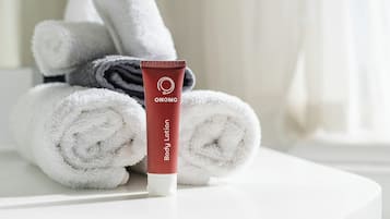 A bathroom with a white sink, a rolled white towel, and a red tube of body lotion.