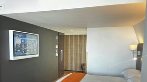Habitación de hotel con cama, una pantalla de televisión mostrando un mensaje de bienvenida y una lámpara fijada a la pared.