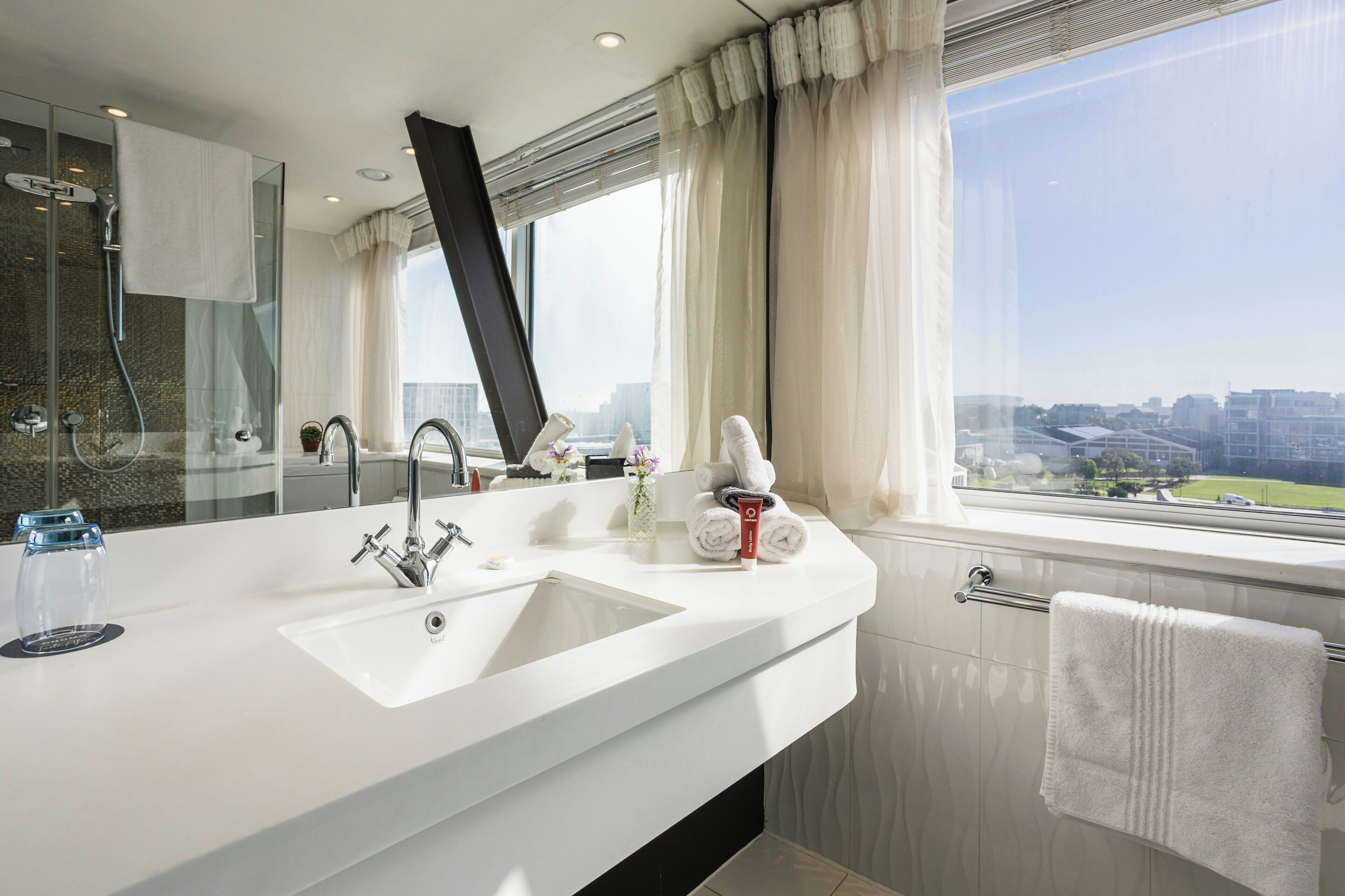 Une salle de bain moderne avec un grand lavabo blanc, un miroir et une fenêtre donnant sur la ville.