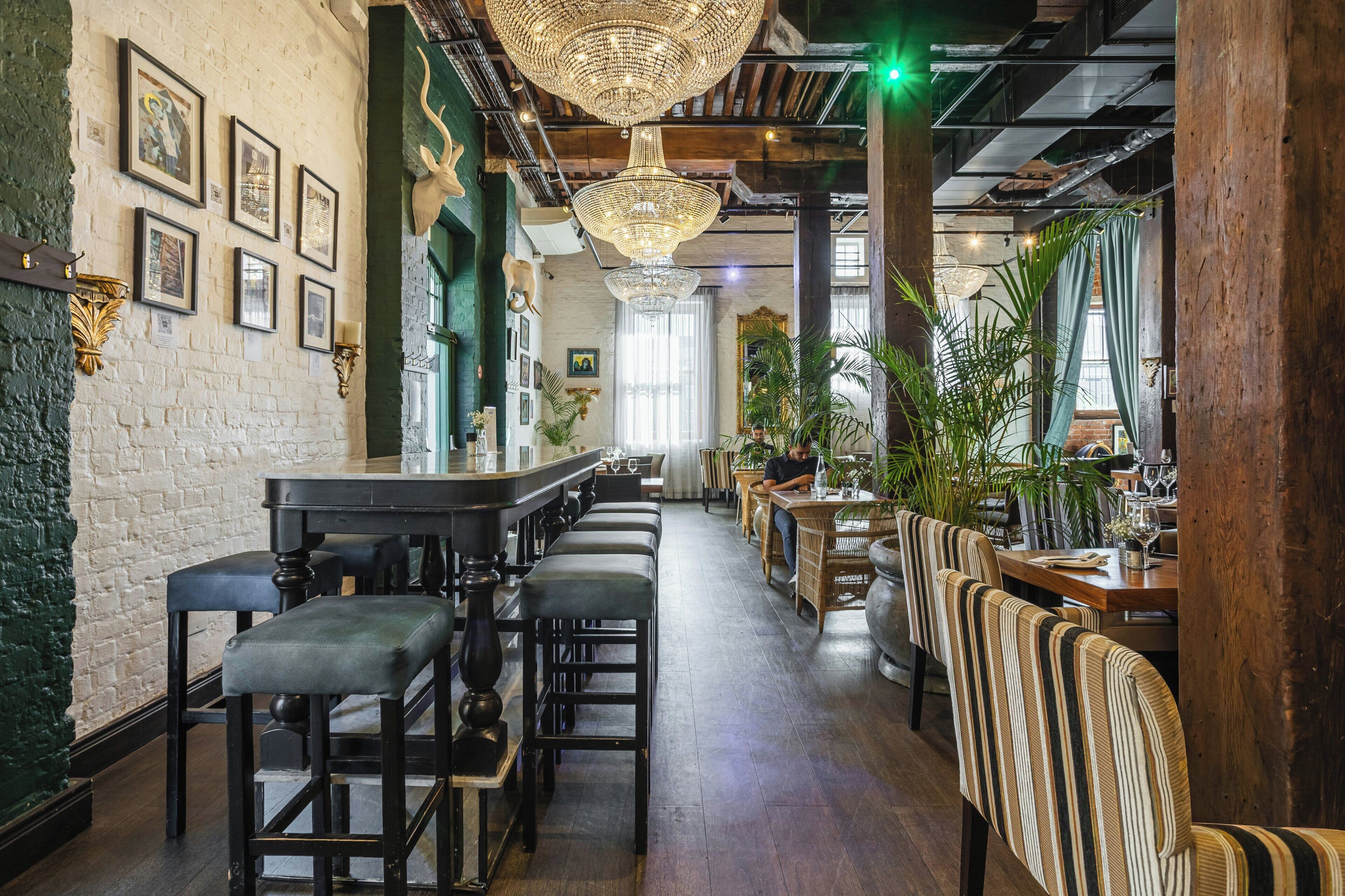 Interior de un restaurante con barra, techo alto con candelabros y vigas de madera.
