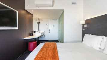 Une chambre d’hôtel comprenant un lit, une table de chevet, un téléviseur fixé au mur, une salle de bain avec un lavabo et un miroir, et un appareil de climatisation.