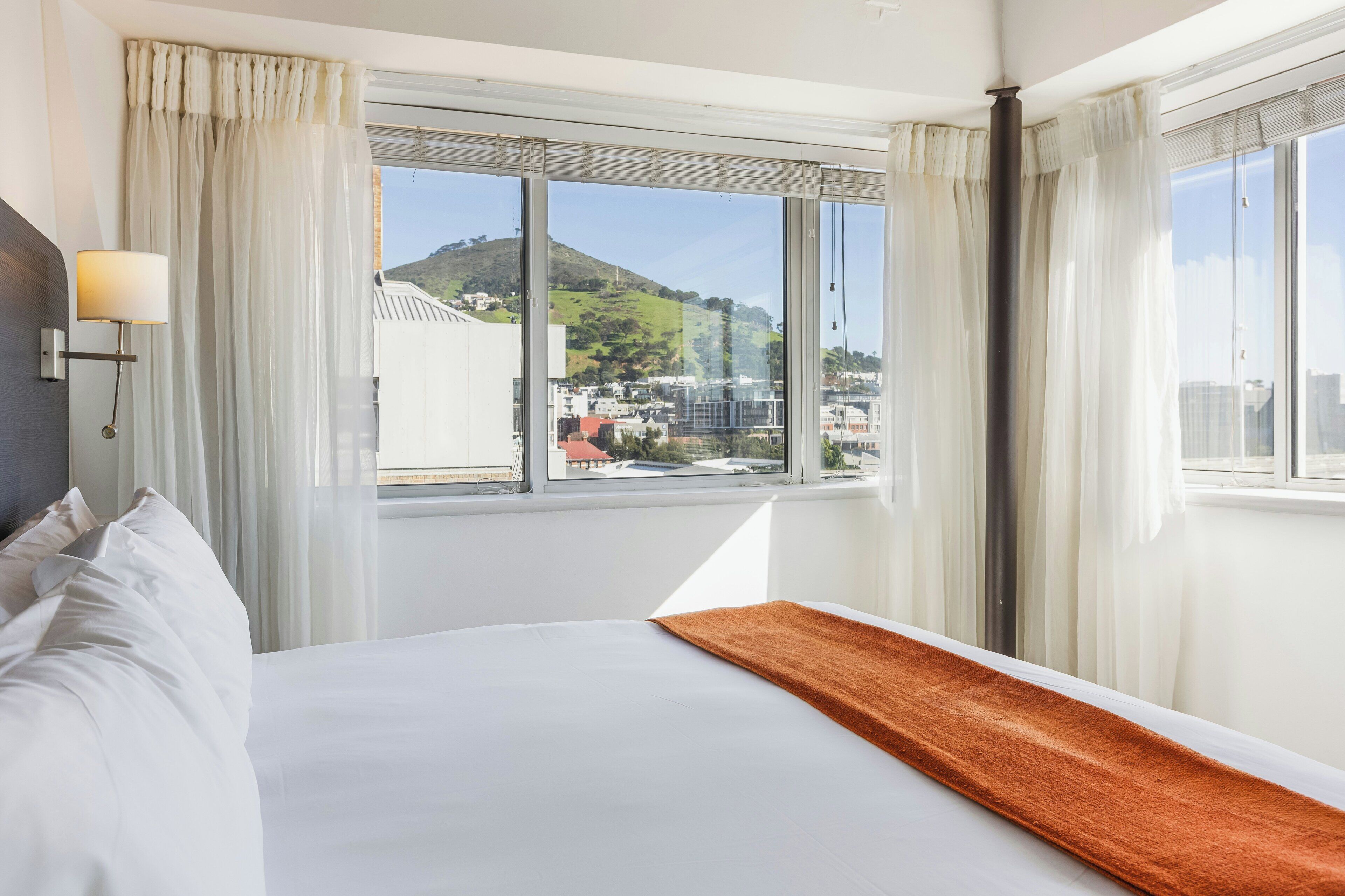 A hotel room with a bed, a window with curtains, and a view of a cityscape.