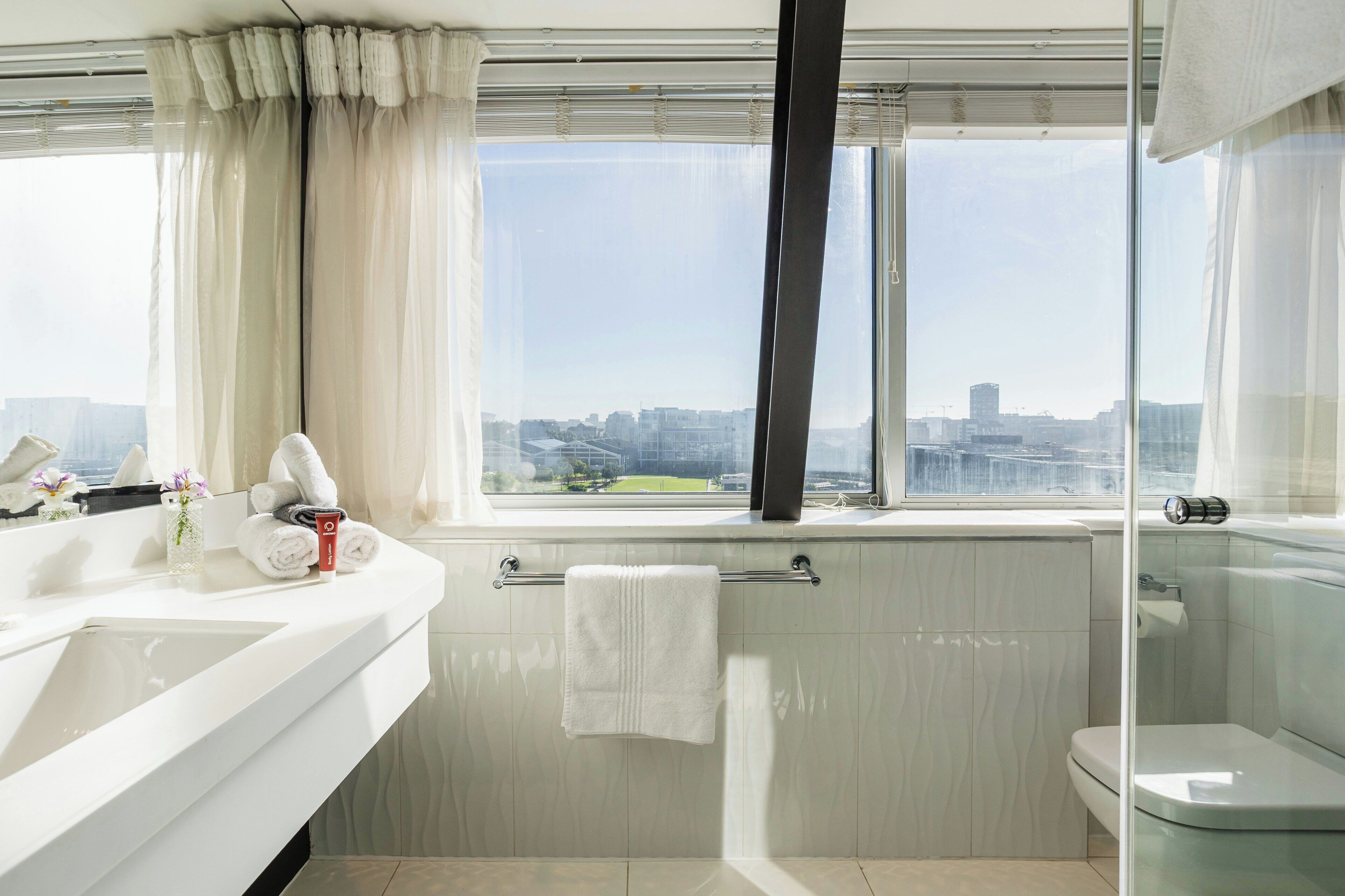 A modern bathroom with a large window, a white sink, and a toilet.