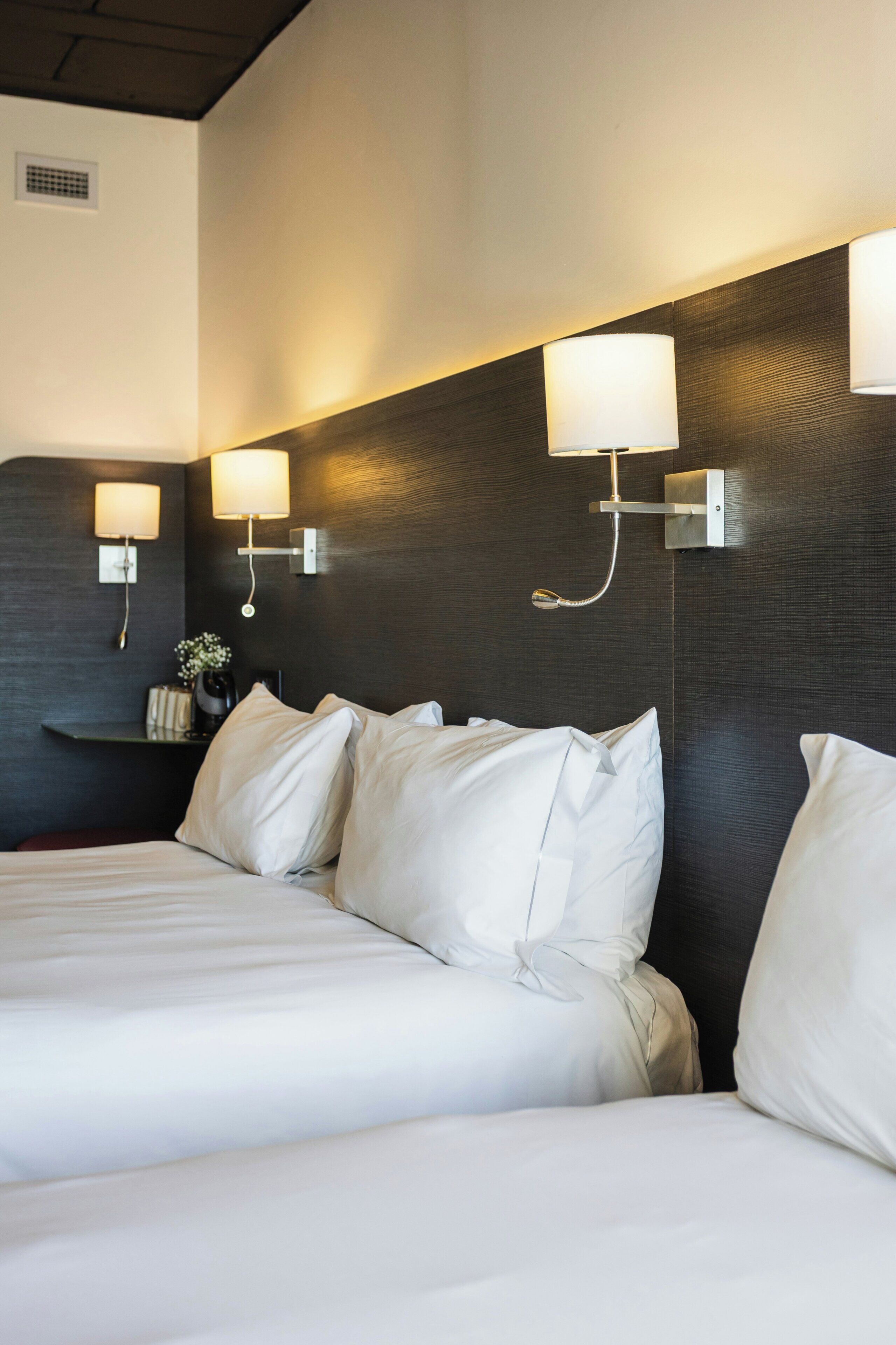 A hotel room with a large bed, two wall-mounted lamps, and a dark textured wall.
