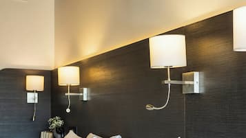 Habitación de hotel con una cama grande, dos lámparas de pared y una pared oscura con textura.
