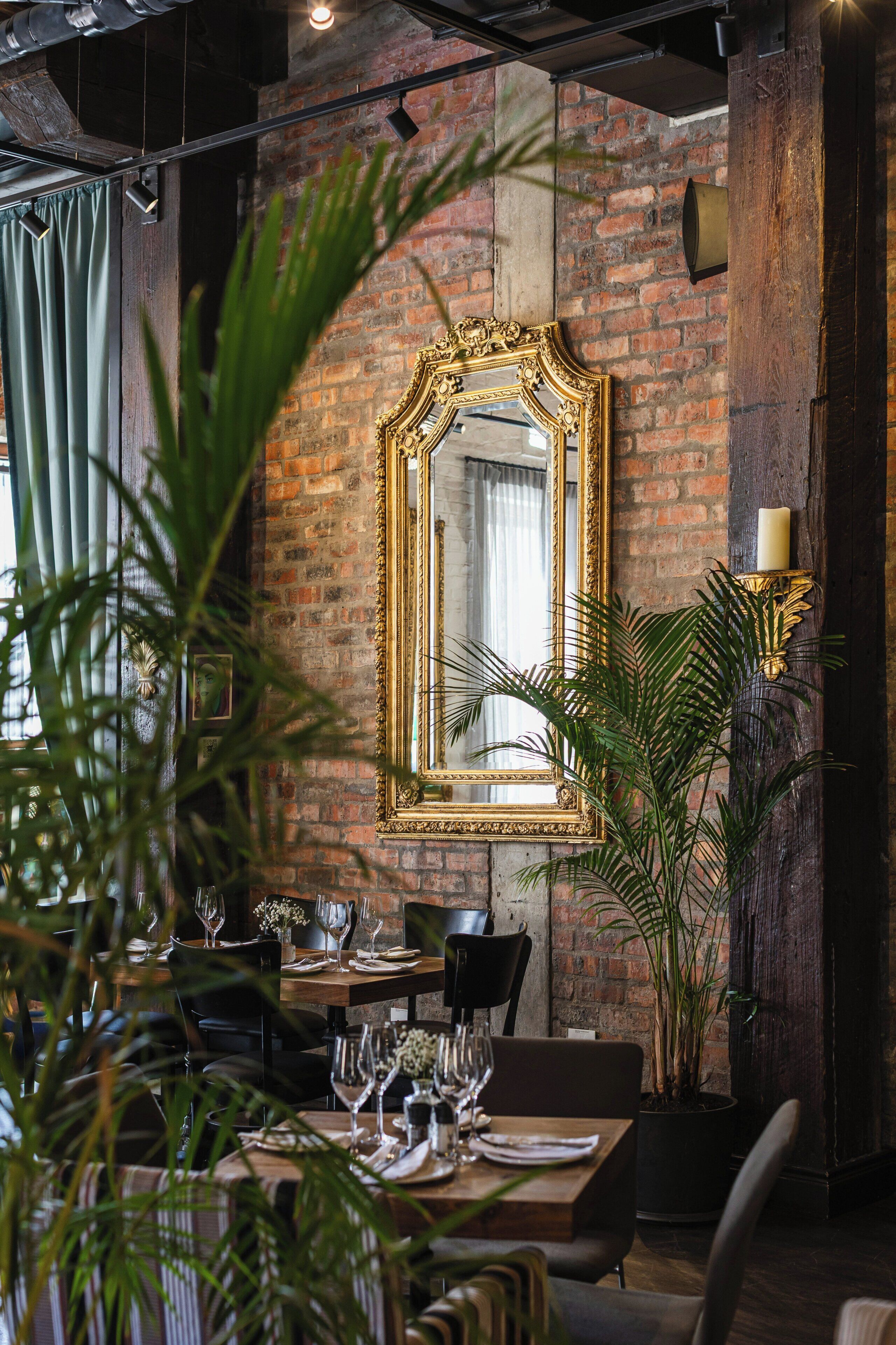 Un comedor con pared de ladrillo, un espejo grande y decorativo, y una vela sobre un atril.