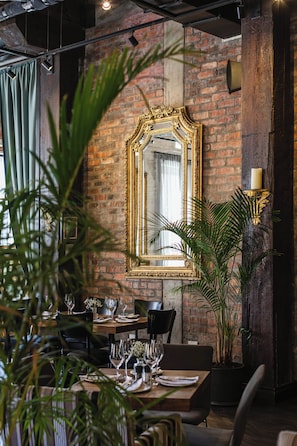 Un comedor con pared de ladrillo, un espejo grande y decorativo, y una vela sobre un atril.