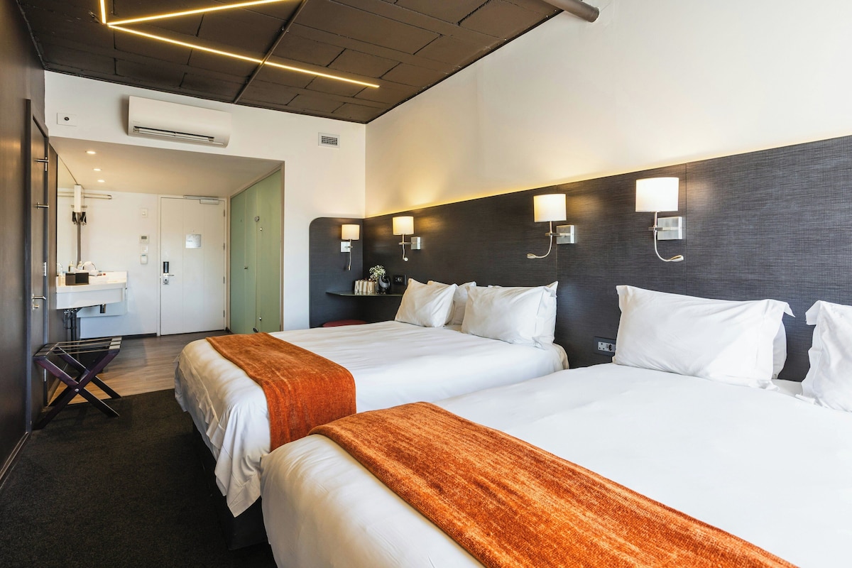 A hotel room with two beds, a bathroom, and a hallway.