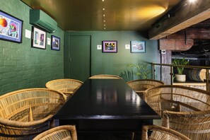 A room with a long black table surrounded by wicker chairs, green walls, and framed artwork. - ONOMO Hotel Waterfront (Cape Town)