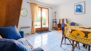 Een kamer met een bank, een eettafel, stoelen, een spiegel en een deur naar een buitengebied.