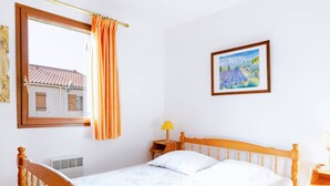 Een slaapkamer met een houten bed, een raam met oranje gordijnen, een nachtkastje met een lamp en een lijst met een schilderij aan de muur.