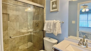 A bathroom with a glass-enclosed shower, a white toilet, and a sink with a modern faucet. - Lani Kai Village 211, Beautifully Remodeled Condo with Indirect Gulf Views! (Gulf Shores)