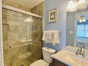 A bathroom with a glass-enclosed shower, a white toilet, and a sink with a modern faucet. - Lani Kai Village 211, Beautifully Remodeled Condo with Indirect Gulf Views! (Gulf Shores)