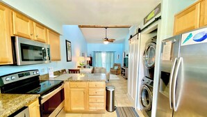 Cocina compacta equipada con microondas, horno y refrigerador, zona de comedor con mesa y sillas, y lavandería con lavadora y secadora.