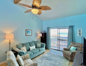 A living room with a sofa, armchairs, a ceiling fan, and a view of the beach through a large window. - Lani Kai Village 211 (Gulf Shores)