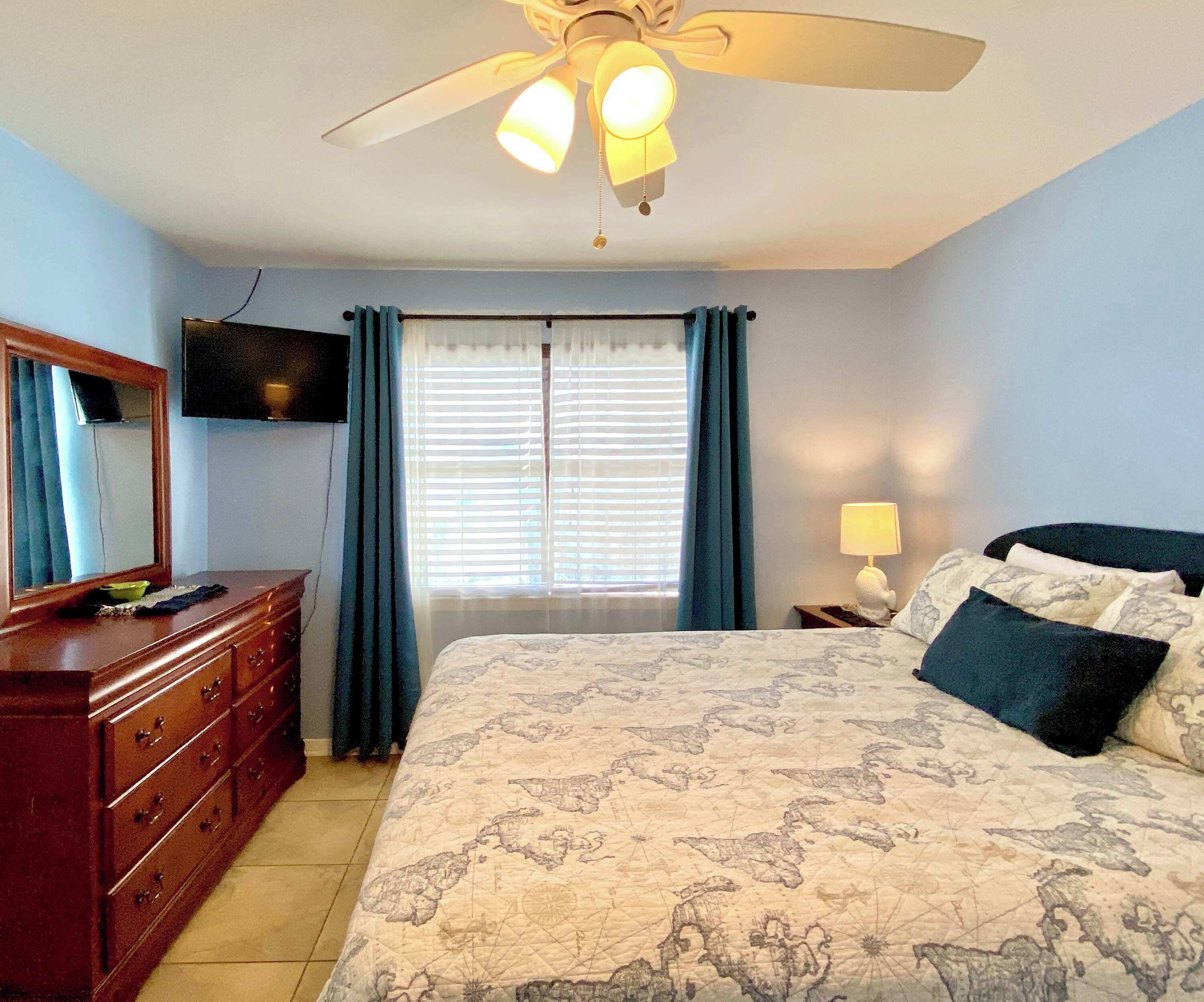 A bedroom with a bed, a dresser, a television, and a ceiling fan.