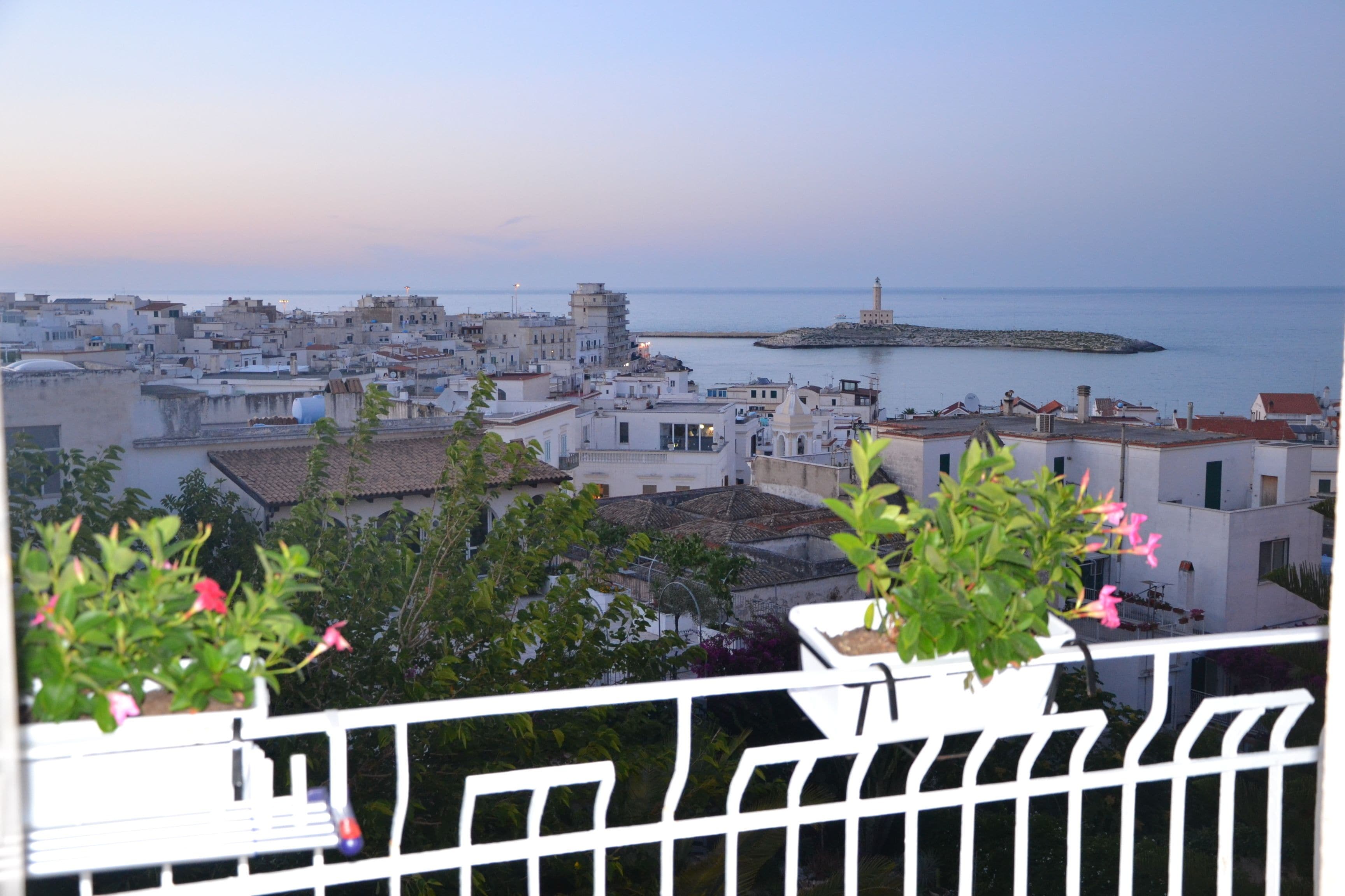 A coastal cityscape with white buildings, a lighthouse, and a view of the sea.