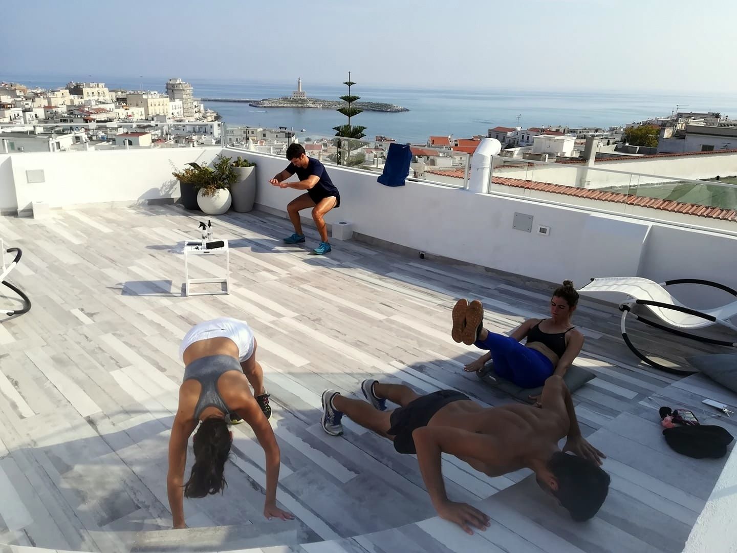 A rooftop with a view of the sea and buildings, featuring exercise equipment and a white chair.